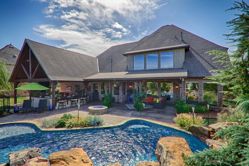 Backyard view of a custom home with a pool, outdoor kitchen, and lush landscaping, showcasing the results of a thoughtful home building process.