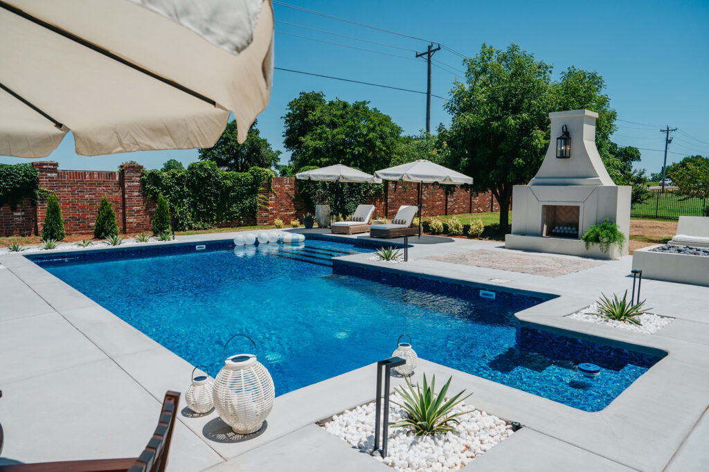 Luxury backyard pool with fireplace and greenery, a refined example of the work of an Oklahoma City Pool Builder.